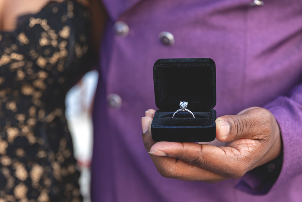 A close-up of a man holding an elegant engagement ring in a black velvet box, showcasing a sparkling diamond