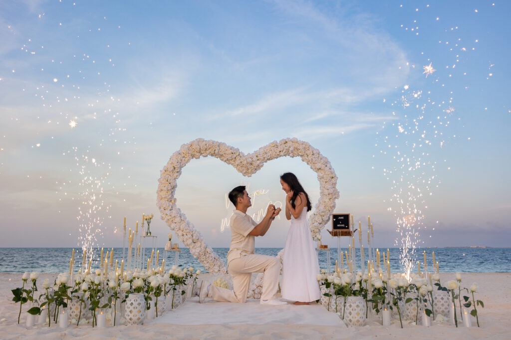Man proposing on one knee at sunset beach setup with fireworks at Secrets Playa Blanca