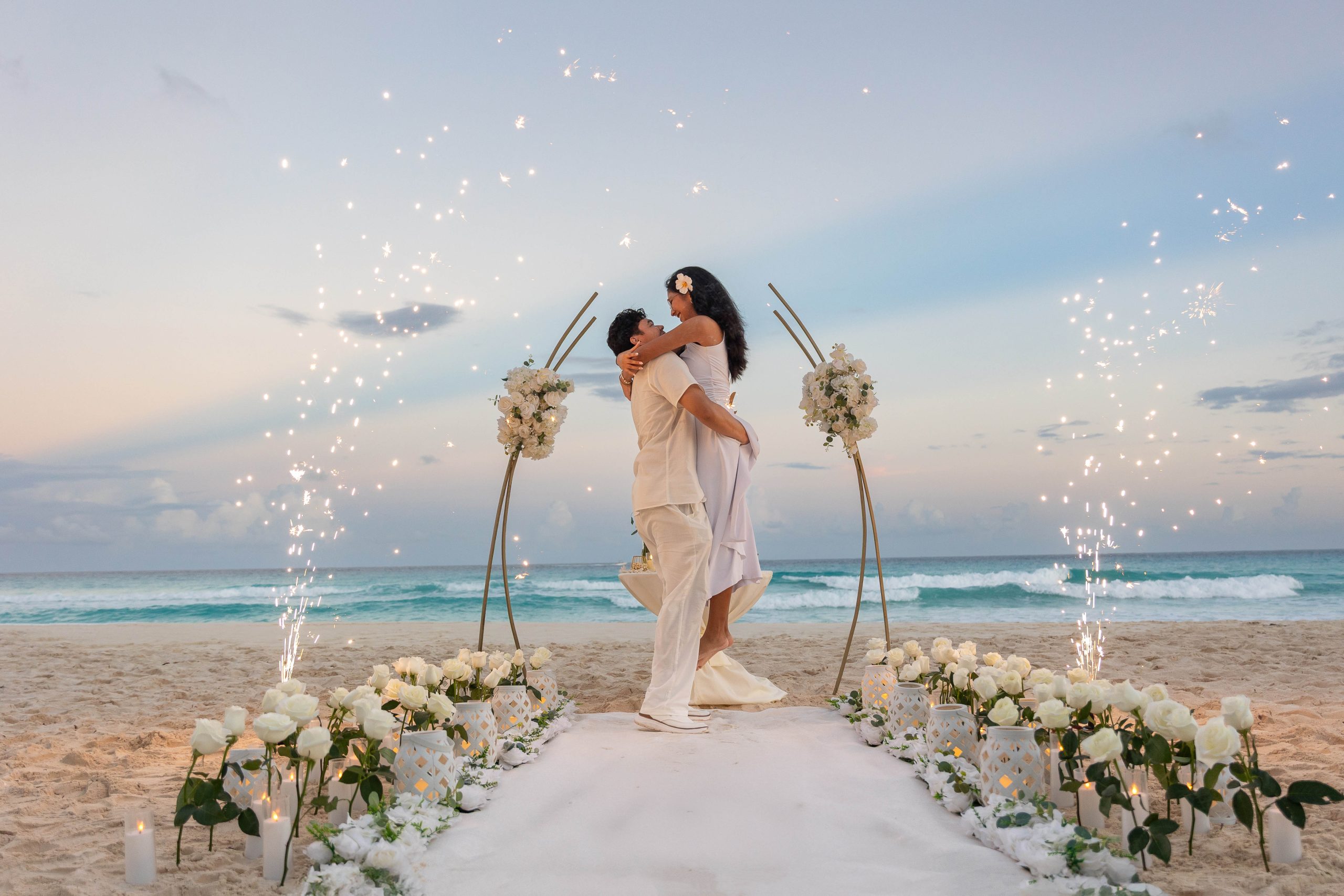 Luxury beach proposal at Riu Kukulkan Cancun with floral aisle, sparklers, and custom arch at sunset