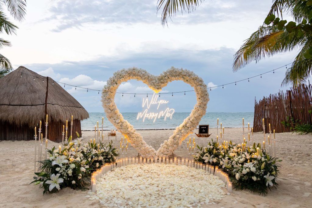 Luxury beach proposal in Mexico with oversized heart-shaped floral arch made of fresh white roses at Acamaya Weddings