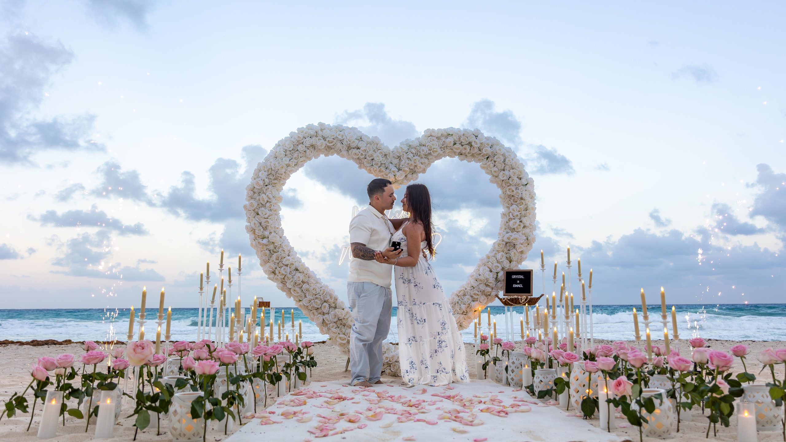 Couple kissing beneath a white rose heart arch during a Cancun proposal